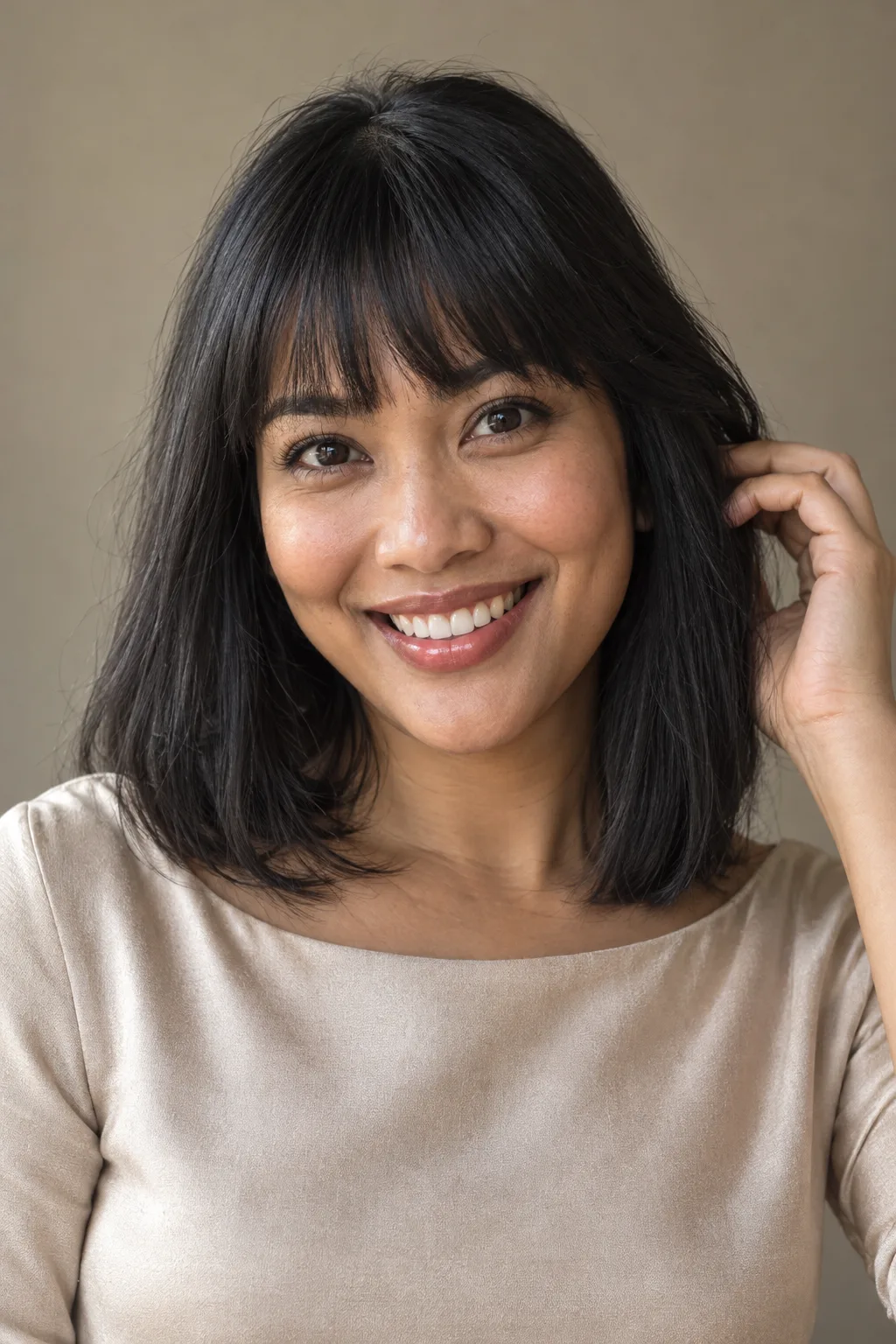 Woman with dark bangs smiling in a champagne top.